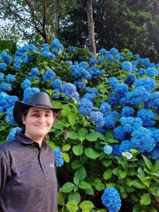 Brianna Erler standing next to blue chrysanthemum flowers.